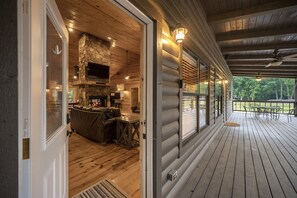 Une cabane en rondins dotée d’une terrasse en bois, d’une cheminée en pierre et d’un salon confortable avec un canapé et une table basse.