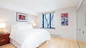 A bedroom with a large bed, a nightstand, a window with a view of trees, and two wall-mounted artworks. - Cozy Couple's Retreat in Downtown Telluride (Telluride)