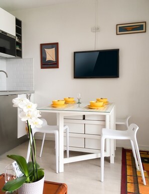 A modern kitchen with white cabinets, a built-in oven, and a dining area with a glass table and white chairs. - Homerez - Flat in Guérande (Guérande)