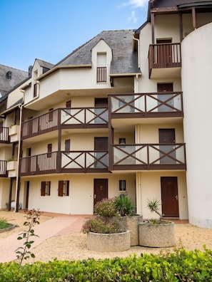A multi-story residential building with balconies, a tiled roof, and a landscaped garden area.