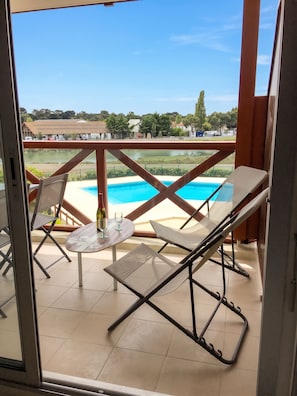 A balcony with a pool view, two lounge chairs, a table, and a bottle of wine.