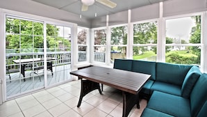 Un solarium con ventilador de techo, ventanas amplias, una mesa y un sofá color turquesa.