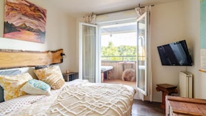 A bedroom with a bed, pillows, a television, and a balcony with a view.