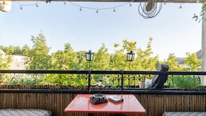 An outdoor seating area with a red table and two cushioned benches, surrounded by a wooden fence and string lights.