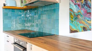 A kitchen with a wooden countertop, a blue backsplash, and a colorful abstract painting on the wall.