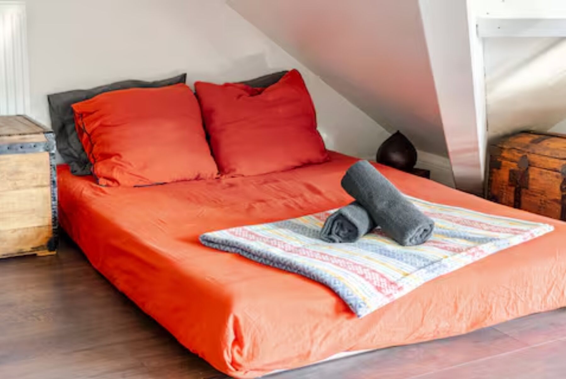 A bed with red bedding, a rolled-up towel, and a striped blanket.