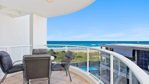 Een balkon met uitzicht op de oceaan, een zwembad en een zithoek met stoelen.
