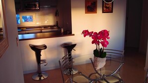 Une cuisine moderne équipée d’un four à micro-ondes, d’un four et d’un petit îlot central. On y trouve deux tabourets de bar et une table en verre sur laquelle est posée une orchidée en pot.