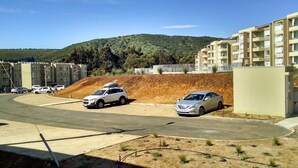 Un espace de stationnement avec deux voitures, un bâtiment doté de balcons et, au loin, un paysage vallonné.