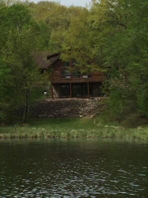 Une cabane dotée d’un balcon donnant sur une étendue d’eau, entourée d’une forêt dense.