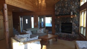 Un acogedor interior de cabaña de madera con chimenea de piedra, mobiliario de madera y vistas al exterior.