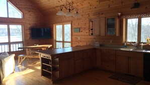 Una cabaña con interior de madera, una cocina con una isla grande, un comedor y un televisor montado en la pared.