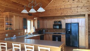 Cocina de cabaña de madera con una isla central, taburetes de bar, un refrigerador y un microondas.