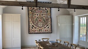 A spacious dining area with a wooden table and chairs, a large tapestry on the wall, and a skylight above. - Stunning 19th century barn conversion in gorgeous Hampshire countryside (South Wonston)