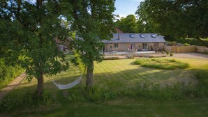 A house with a sloped roof, a patio with outdoor furniture, and a well-maintained lawn. - Stunning 19th century barn conversion in gorgeous Hampshire countryside (South Wonston)