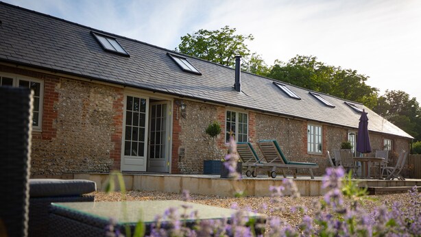 A stone building with a sloped roof, large windows, and outdoor seating. - Stunning 19th century barn conversion in gorgeous Hampshire countryside (South Wonston)