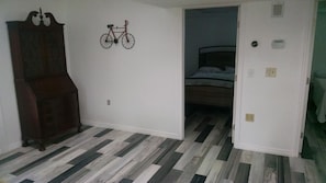 A room with a herringbone-patterned floor, a wooden armoire, a wall-mounted bicycle decoration, and a bed in the adjacent room.