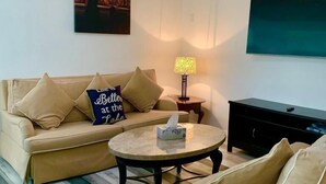 Un salon avec un canapé beige, une table basse ronde et un téléviseur fixé au mur.