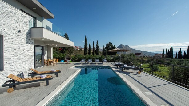 A modern pool area with lounge chairs and a dining set, surrounded by a wooden deck and a stone wall. - Villa Domenica with Heated Pool (Solin)