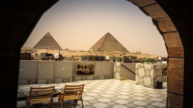 A view of two pyramids through an archway, with a table and chairs in the foreground. - Queen Pyramids View Inn (Giza)