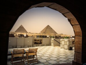 A view of two pyramids through an archway, with a table and chairs in the foreground. - Queen Pyramids View Inn (Giza)