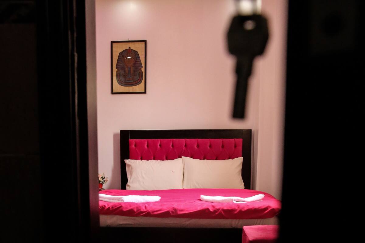 A bedroom with a red bedspread, white pillows, and a red floral rug.