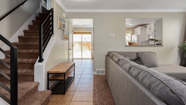 A staircase with a wooden bench, a grey sofa, and a kitchen area in the background. - The Lake View: Family and business travel (Lehi)