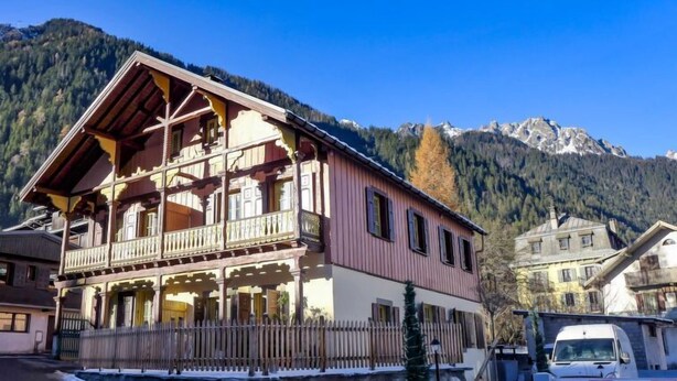 A two-story wooden building with balconies, a stone wall, and a snow-covered ground. - Le Chalet Suisse by Interhome (Chamonix)