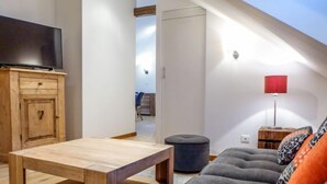 A modern living room with a wooden coffee table, grey sofa with patterned cushions, a red floor lamp, and a TV on a wooden cabinet. - Le Chalet Suisse by Interhome (Chamonix)