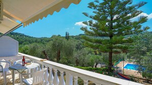 Un balcone con sedie e tavolo bianchi, vista su una piscina e una vegetazione rigogliosa.