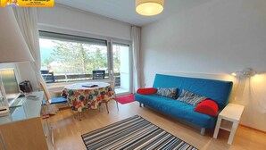 Un salon moderne avec un canapé bleu, une petite table et une fenêtre donnant sur des arbres.