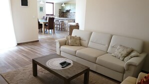 Ein Wohnzimmer mit einem beigen Sofa, einem Holztisch und einer Küche im Hintergrund.