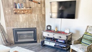 A cozy living room with a fireplace, a television, a wooden coffee table, and patterned furniture. - Cozy, updated 2 Bedroom / 2 Bathroom condo (Steamboat Springs)