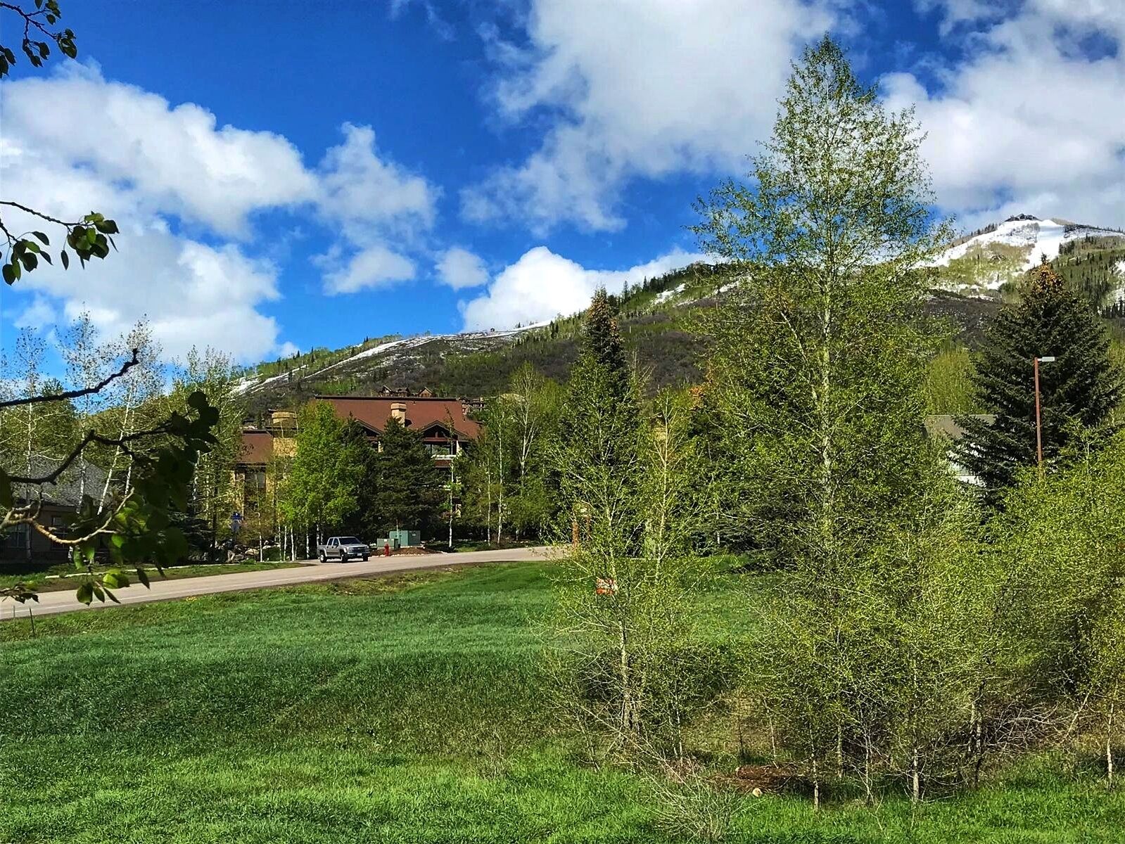 Un hotel con montañas al fondo, un estacionamiento y un campo de césped.