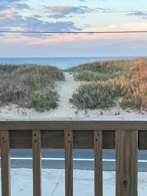 Ein Sandweg am Strand, der zum Meer führt, aufgenommen aus der Perspektive einer Holzbrüstung.