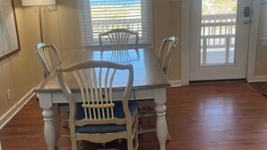 A dining area with a wooden table and chairs, a ceiling fan, and a view of the beach through a window. - Classic, semi ocean front OBX cottage steps away from the beach. (Kitty Hawk)