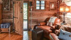 A rustic cabin interior with wooden walls, a leather sofa, a small table, and a lamp. - Historic Log Cabin, Yard, Firepit, Fireplace, WIFI , Private (Maggie Valley)