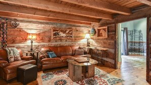 A rustic wooden interior with a leather sofa, wooden coffee table, and patterned rug. - Historic Log Cabin, Yard, Firepit, Fireplace, WIFI , Private (Maggie Valley)