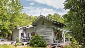 A rustic log cabin with a porch, surrounded by lush greenery and trees. - Historic Log Cabin, Yard, Firepit, Fireplace, WIFI , Private (Maggie Valley)