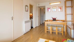 Ein Zimmer mit einem Holzesstisch, Stühlen, einer kleinen Küche und einer weißen Tür.