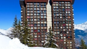 Ein Hochhaus-Hotel mit mehreren Balkonen, umgeben von schneebedeckten Bergen und immergrünen Bäumen.