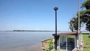 A lakeside structure with a glass enclosure, a wooden deck, and a tall pole.