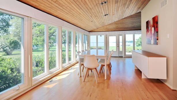 A spacious room with large windows, wooden ceiling, and a white dining table with chairs.