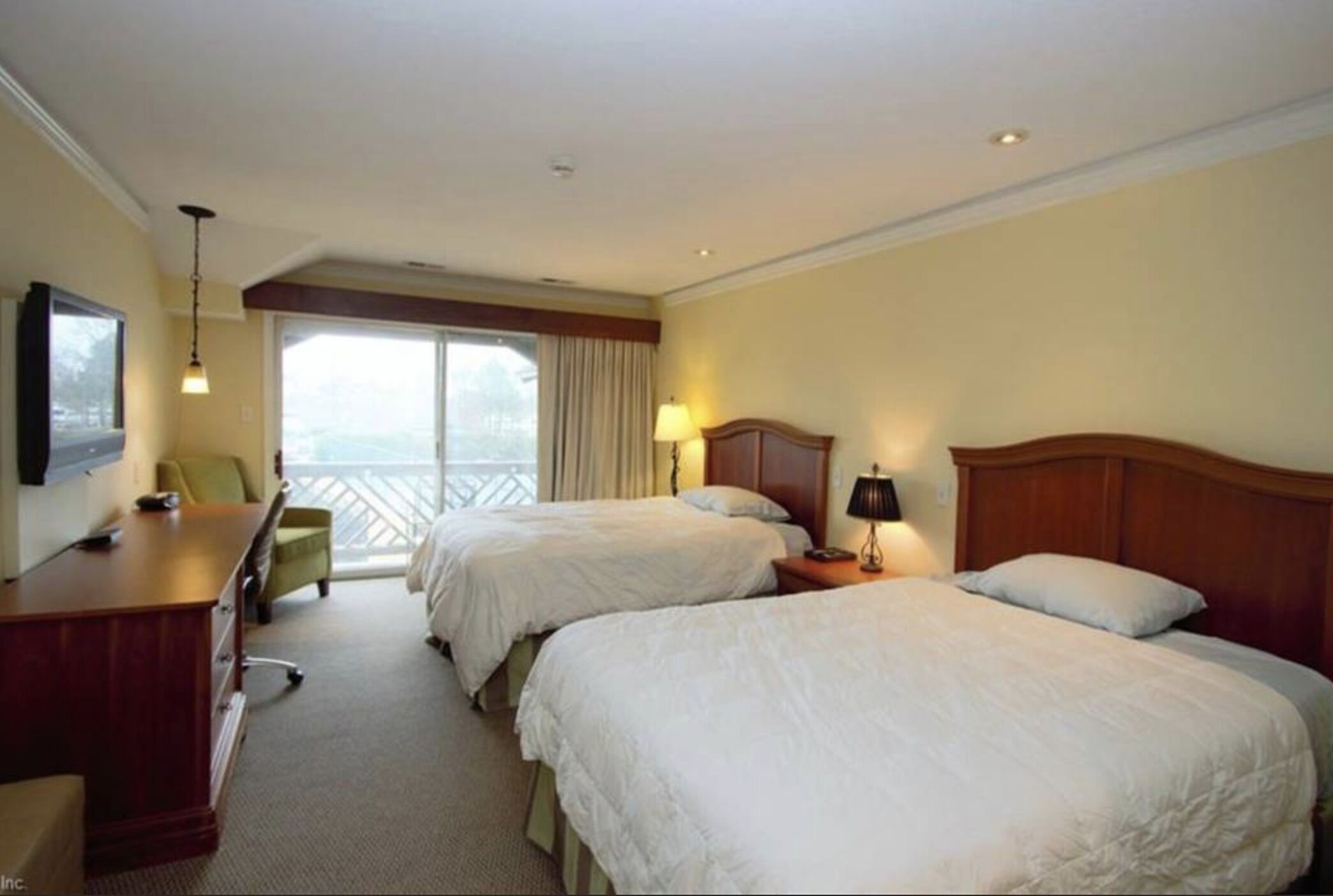 Een hotelkamer met twee bedden, een bureau, een stoel en een balkon met gordijnen.