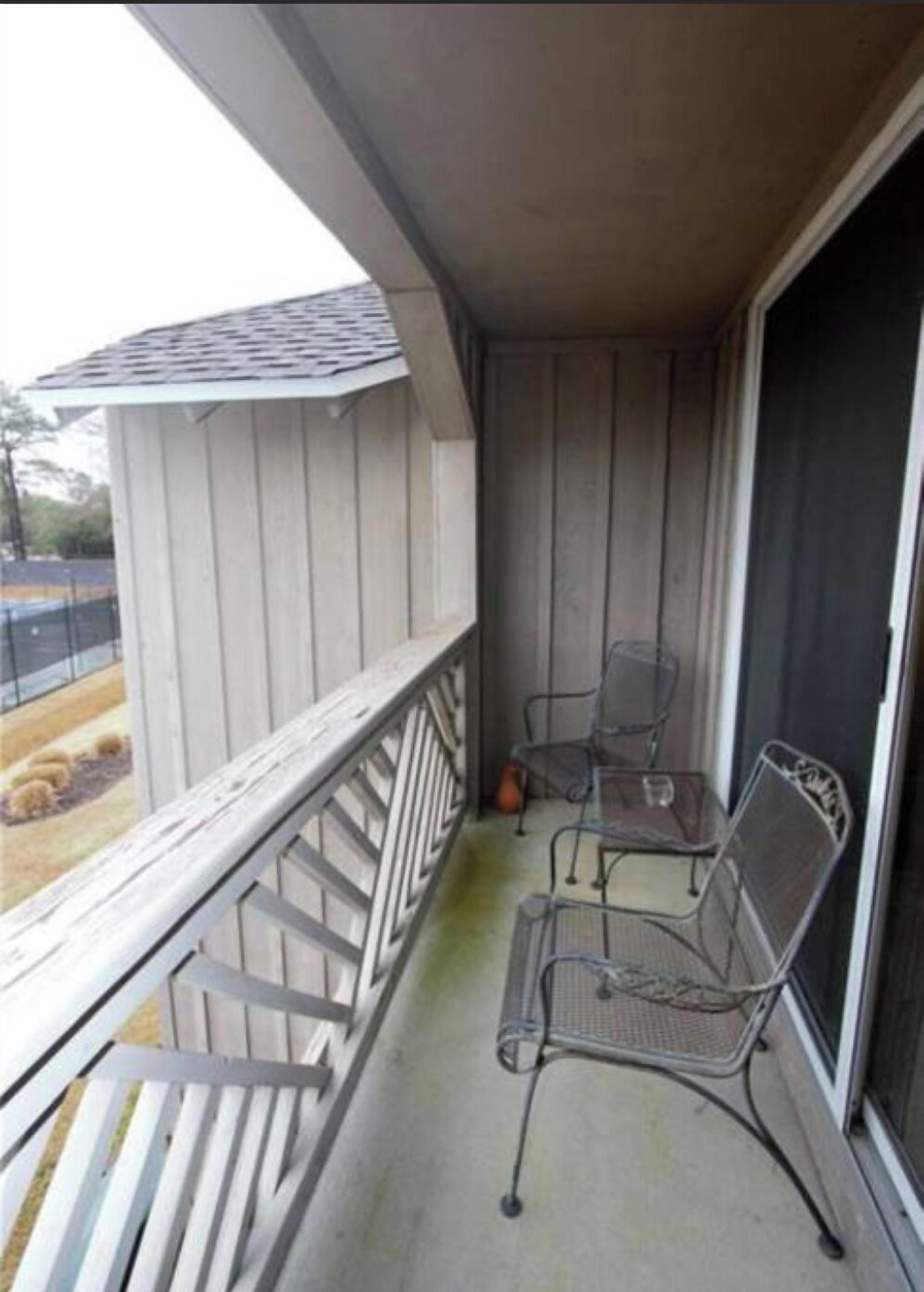 A balcony with two metal chairs and a small table, a wooden railing, and a view of a fenced area with hay bales.