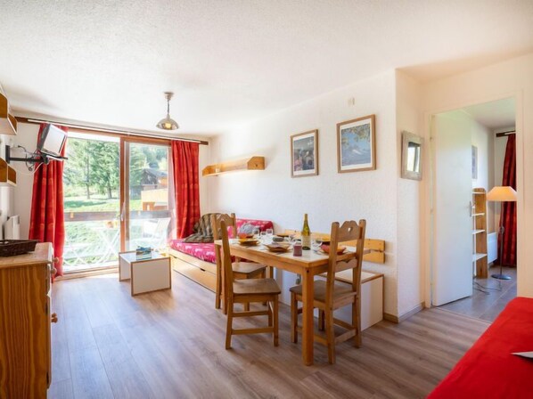 Ein Essbereich mit Holztisch und Stühlen, einem roten Sofa und Blick durch eine Glastür auf eine Terrisse.