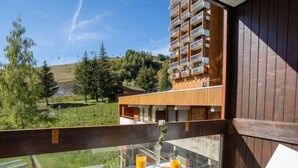 Varanda com mesa posta para o café da manhã, com vista para um edifício moderno e uma paisagem montanhosa.