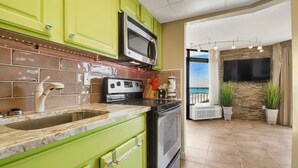 Una cocina con gabinetes verdes, un microondas de acero inoxidable, una estufa a gas y un amplio ventanal con vistas a un balcón.