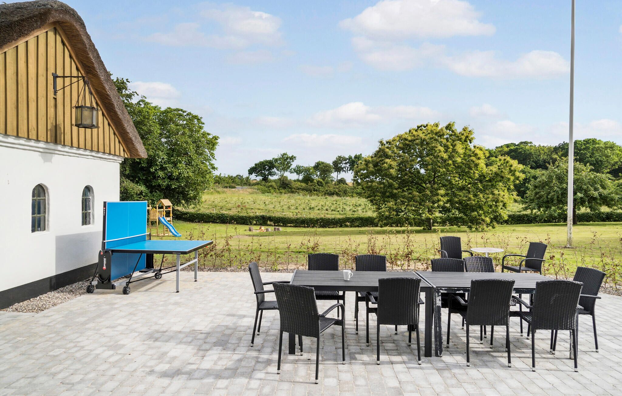A patio area with a table and chairs, a play structure, and a building with a thatched roof.