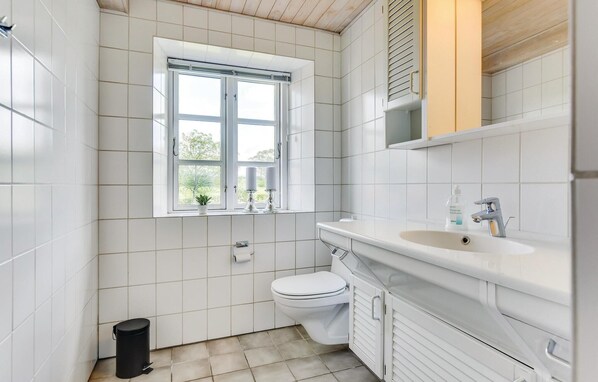 A small, clean bathroom with white tiles, a toilet, a sink with a mirror, and a window with a view of greenery. - Gorgeous home in Haderslev with WiFi (Haderslev)